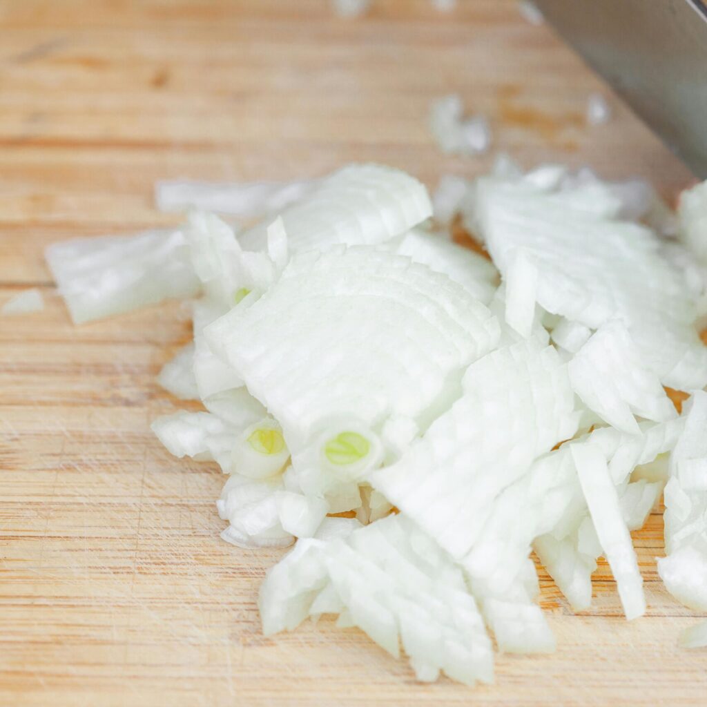 Knife slicing onions on a wooden cutting board, preparing ingredients for a meal.