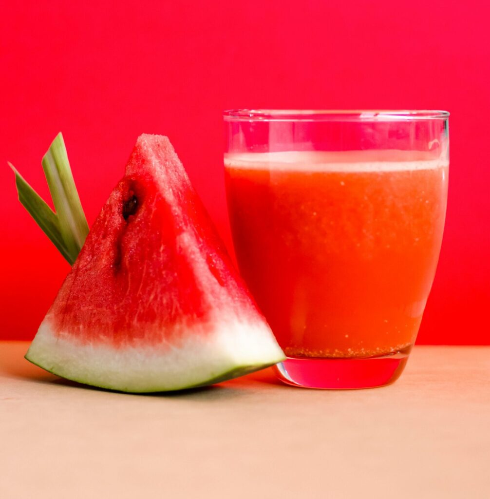 Refreshing watermelon juice and slice against a vibrant red background, perfect for summer vibes.