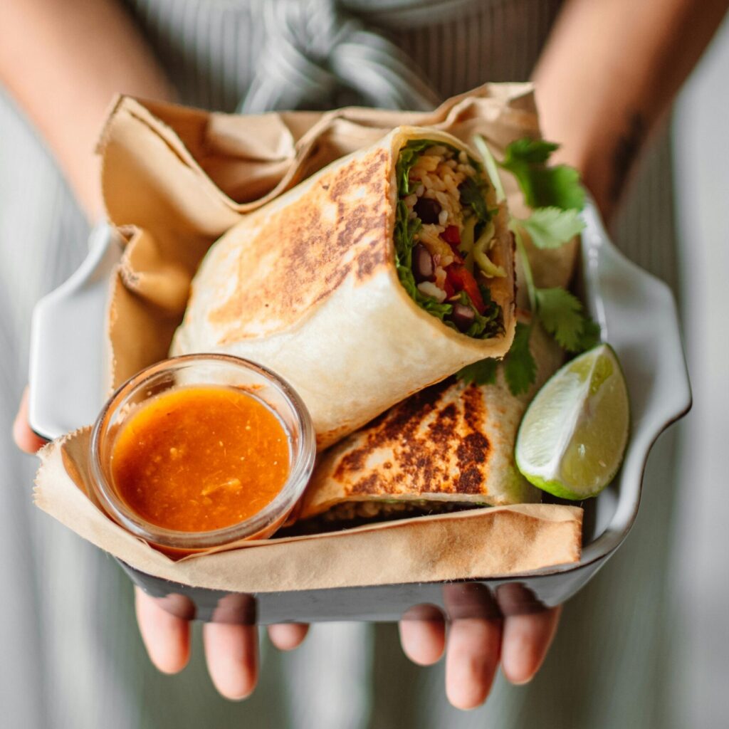 Colorful Mexican burrito with tangy sauce and lime wedge, served elegantly.