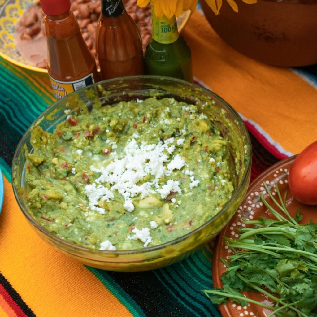 Colorful Mexican feast with fresh guacamole, sunflowers, and vibrant ingredients on a table.